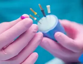 Close-up of gloved hands holding a small dental instrument holder containing multiple color-coded dental burs or tips.